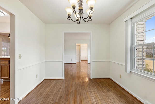 unfurnished room featuring a healthy amount of sunlight, hardwood / wood-style flooring, and a notable chandelier