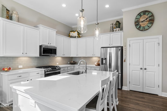 kitchen with a center island with sink, sink, white cabinetry, stainless steel appliances, and light stone counters