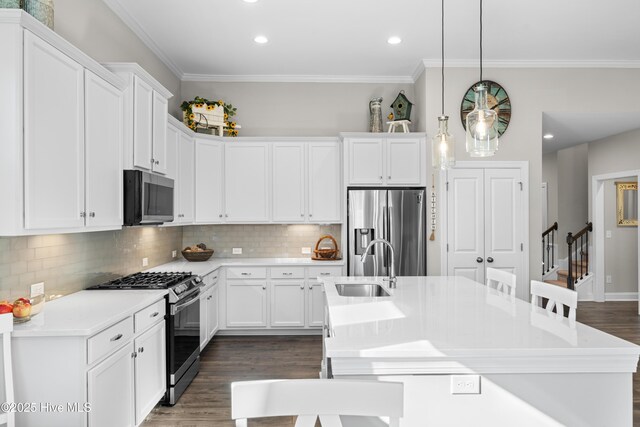 kitchen featuring hanging light fixtures, white cabinets, stainless steel appliances, and a kitchen island with sink