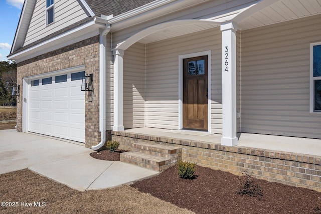 doorway to property with a garage, brick siding, a porch, and a shingled roof