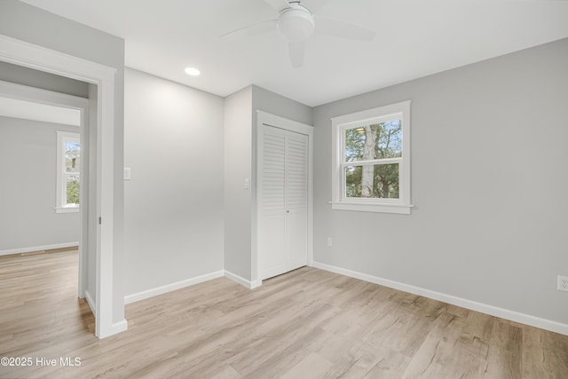 unfurnished bedroom with ceiling fan, a closet, multiple windows, and light wood-type flooring