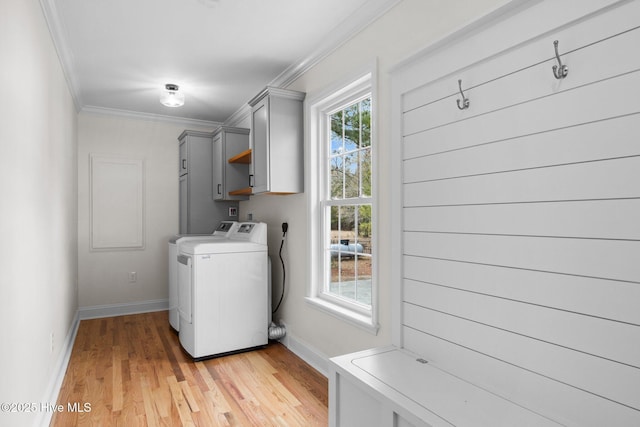 clothes washing area with washing machine and clothes dryer, light hardwood / wood-style flooring, ornamental molding, and cabinets