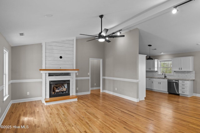 unfurnished living room with ceiling fan, sink, a fireplace, vaulted ceiling with beams, and light hardwood / wood-style floors