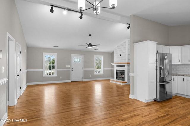 unfurnished living room with a fireplace, rail lighting, high vaulted ceiling, light hardwood / wood-style flooring, and ceiling fan with notable chandelier