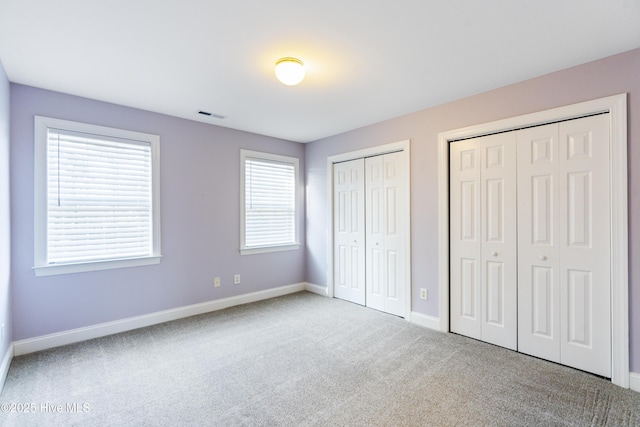 unfurnished bedroom with multiple closets and light colored carpet