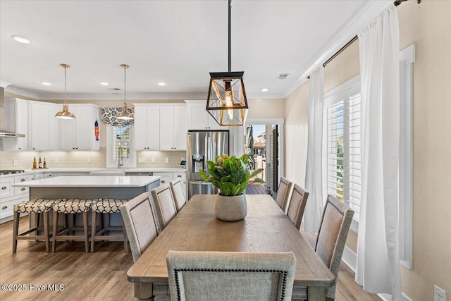 dining room featuring light wood-style floors, visible vents, crown molding, and recessed lighting