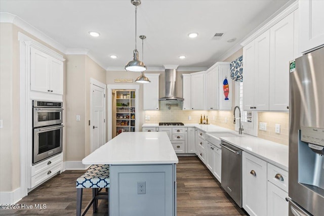 kitchen featuring a breakfast bar area, visible vents, appliances with stainless steel finishes, a sink, and wall chimney exhaust hood