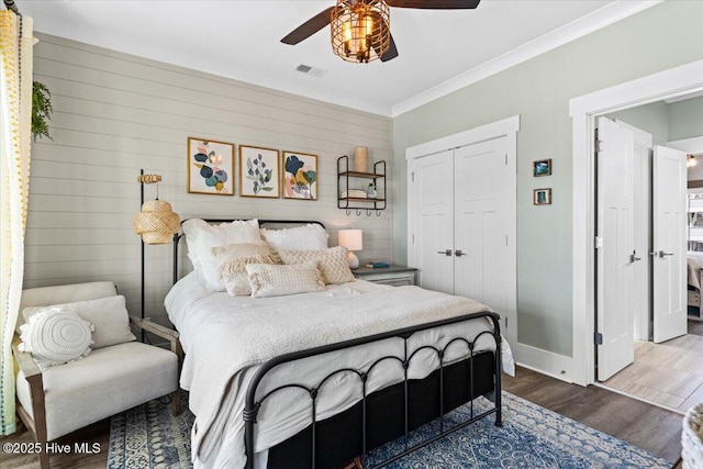 bedroom with crown molding, a closet, visible vents, wood finished floors, and baseboards