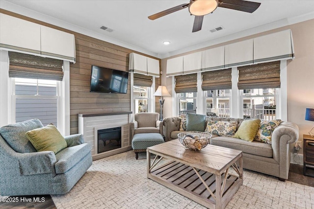 living room featuring a glass covered fireplace, visible vents, wood walls, and ceiling fan