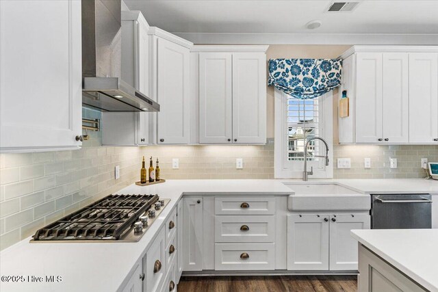 kitchen featuring visible vents, white cabinets, appliances with stainless steel finishes, wall chimney range hood, and a sink