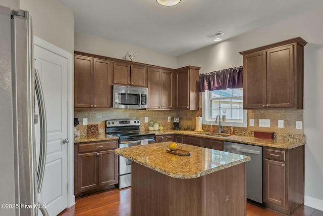 kitchen featuring hardwood / wood-style flooring, appliances with stainless steel finishes, sink, light stone counters, and a center island