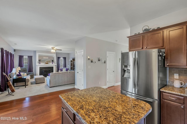 kitchen featuring dark wood-type flooring, stone countertops, stainless steel fridge, backsplash, and ceiling fan