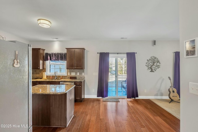 kitchen featuring light stone countertops, dark brown cabinetry, tasteful backsplash, sink, and stainless steel fridge