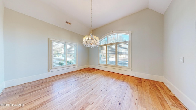 empty room featuring lofted ceiling, light wood-type flooring, and a notable chandelier