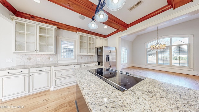 kitchen featuring stainless steel fridge, decorative backsplash, black electric cooktop, decorative light fixtures, and white cabinets