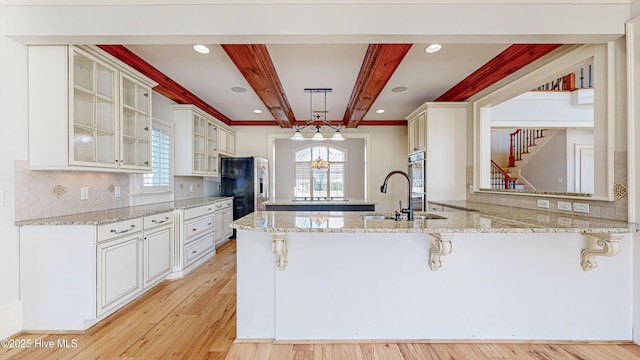 kitchen with light stone countertops, decorative light fixtures, kitchen peninsula, and beamed ceiling