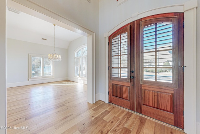 foyer entrance with lofted ceiling, french doors, an inviting chandelier, and light hardwood / wood-style floors