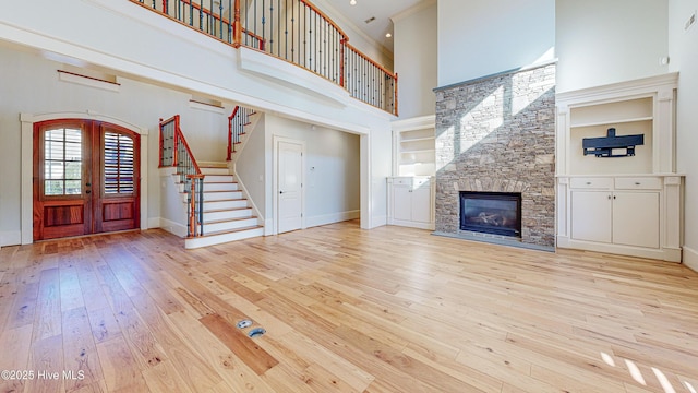 unfurnished living room with french doors, a fireplace, a high ceiling, and light hardwood / wood-style flooring