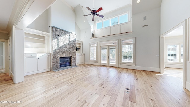 unfurnished living room featuring a high ceiling, a wealth of natural light, a fireplace, light hardwood / wood-style floors, and ceiling fan