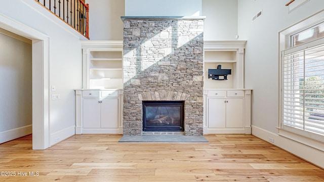 unfurnished living room with a towering ceiling, light hardwood / wood-style flooring, and a stone fireplace