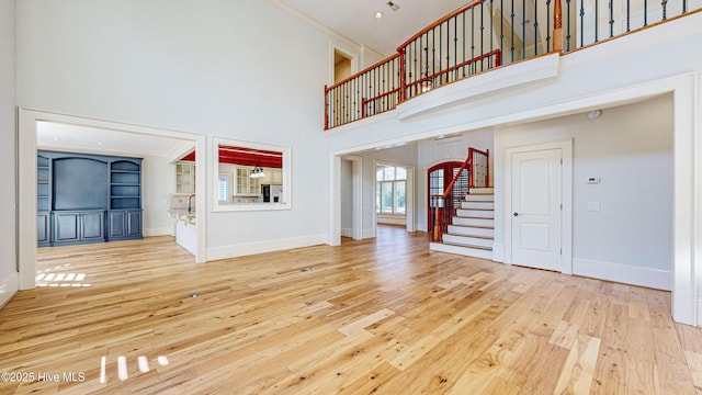 unfurnished living room featuring built in features, a towering ceiling, and light hardwood / wood-style floors