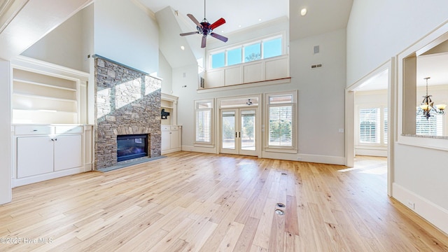 unfurnished living room with ceiling fan with notable chandelier, a towering ceiling, built in shelves, a fireplace, and light wood-type flooring