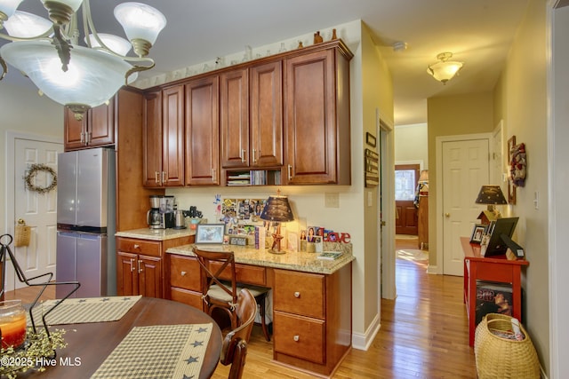 kitchen with light stone counters, light hardwood / wood-style flooring, a chandelier, and stainless steel refrigerator