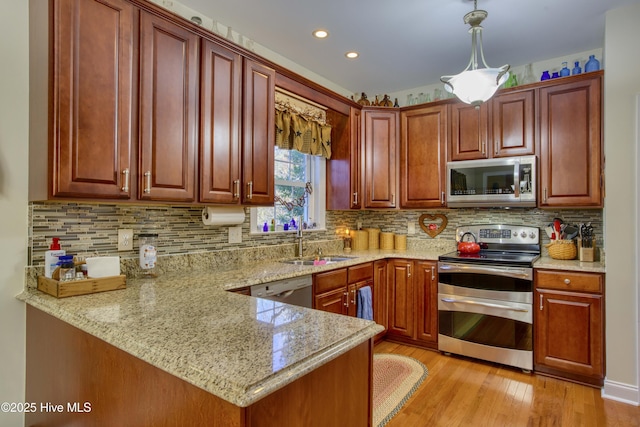 kitchen with pendant lighting, kitchen peninsula, sink, light stone countertops, and stainless steel appliances