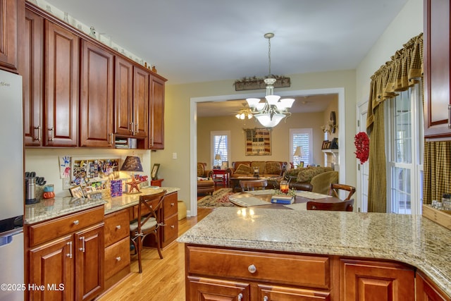 kitchen featuring decorative light fixtures, fridge, an inviting chandelier, light hardwood / wood-style flooring, and light stone countertops