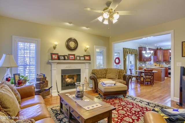 living room with light wood-type flooring and ceiling fan with notable chandelier