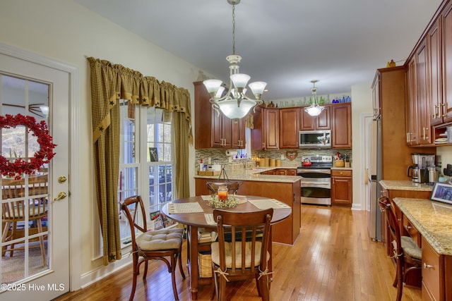 kitchen featuring light hardwood / wood-style floors, appliances with stainless steel finishes, a notable chandelier, hanging light fixtures, and light stone counters