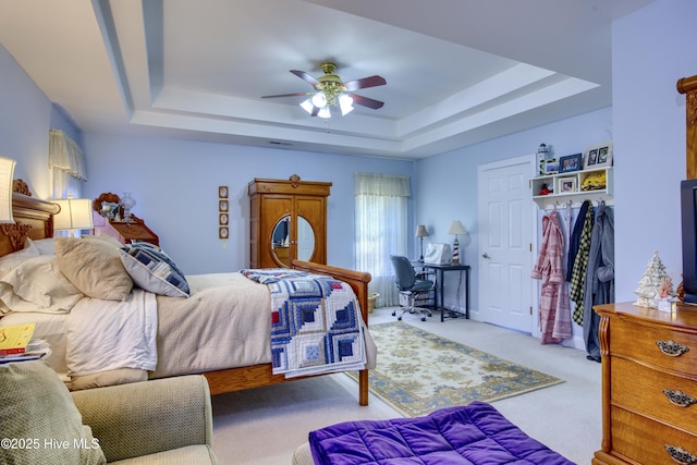 bedroom featuring ceiling fan, light carpet, and a tray ceiling