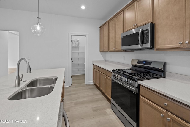 kitchen with sink, light hardwood / wood-style flooring, hanging light fixtures, light stone countertops, and stainless steel appliances