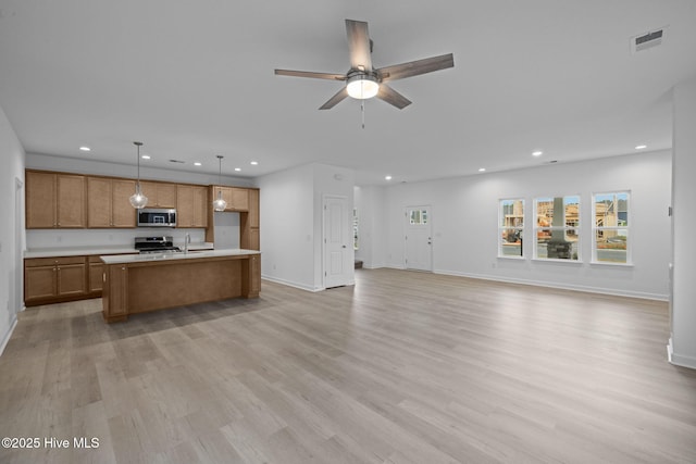 kitchen featuring light wood-type flooring, stainless steel appliances, pendant lighting, and a kitchen island with sink