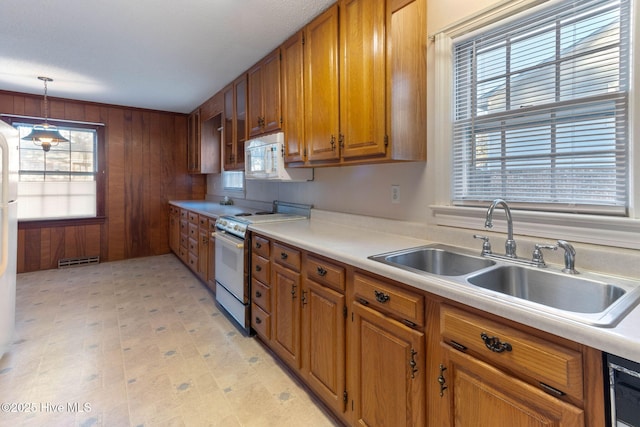 kitchen with sink, white appliances, wooden walls, and hanging light fixtures