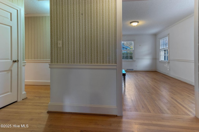 corridor with a textured ceiling, light hardwood / wood-style flooring, and ornamental molding