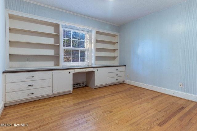 unfurnished office with built in desk, light hardwood / wood-style floors, and built in shelves