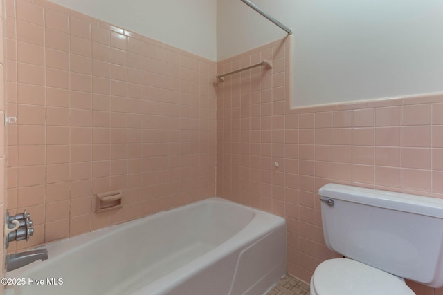 bathroom featuring toilet, tiled shower / bath, tile walls, and tile patterned floors