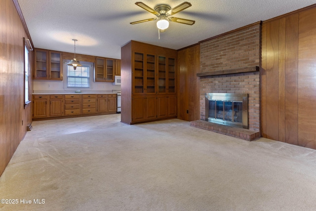 unfurnished living room with light colored carpet, a brick fireplace, wooden walls, and a textured ceiling