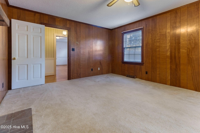 carpeted spare room featuring ceiling fan, a textured ceiling, and wood walls