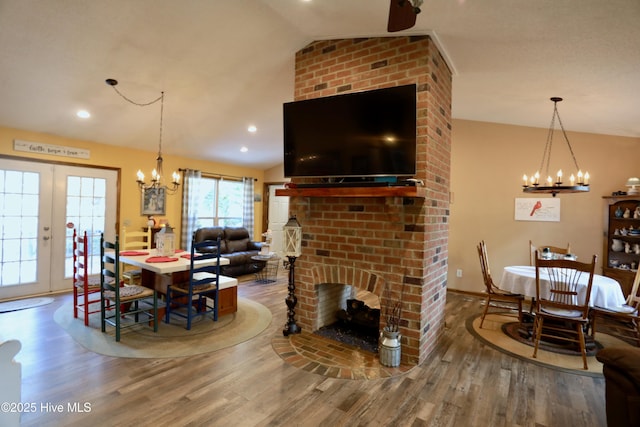 dining area with hardwood / wood-style floors, a fireplace, lofted ceiling, an inviting chandelier, and french doors