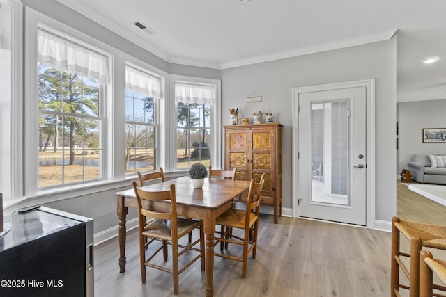 dining area with a healthy amount of sunlight, light wood-type flooring, and ornamental molding