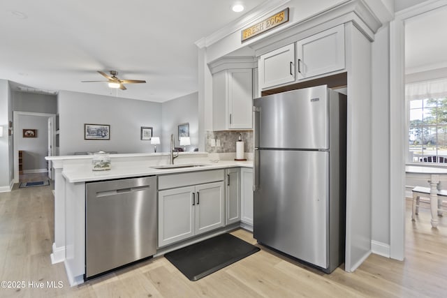 kitchen with appliances with stainless steel finishes, tasteful backsplash, sink, kitchen peninsula, and light hardwood / wood-style flooring