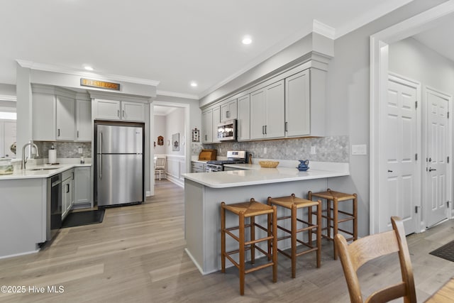 kitchen with appliances with stainless steel finishes, sink, ornamental molding, kitchen peninsula, and gray cabinetry