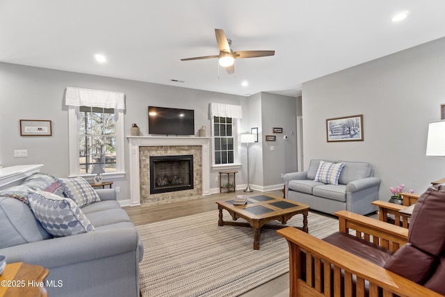 living room with ceiling fan, light wood-type flooring, and a tiled fireplace