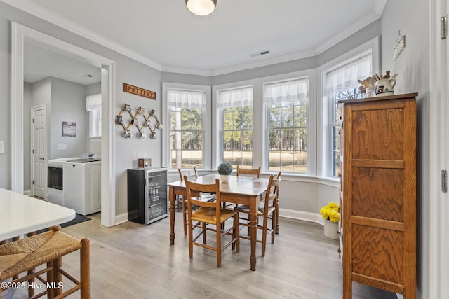 dining room with light wood-type flooring, washer and dryer, wine cooler, and ornamental molding