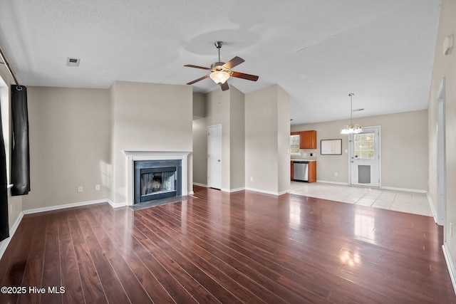 unfurnished living room with lofted ceiling, a fireplace with flush hearth, wood finished floors, baseboards, and ceiling fan with notable chandelier