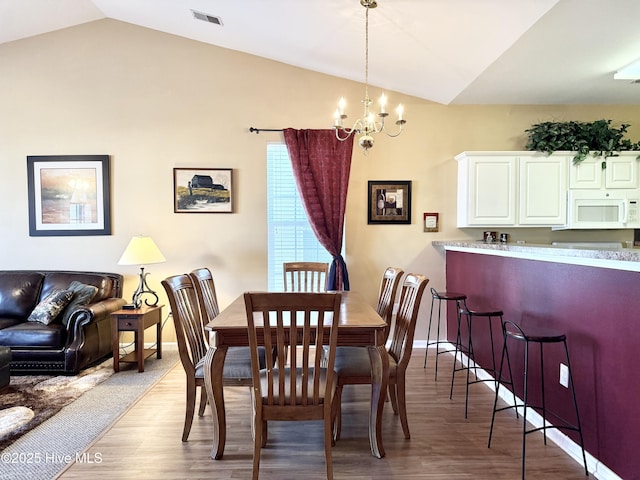 dining space featuring light wood-type flooring, visible vents, baseboards, lofted ceiling, and a chandelier