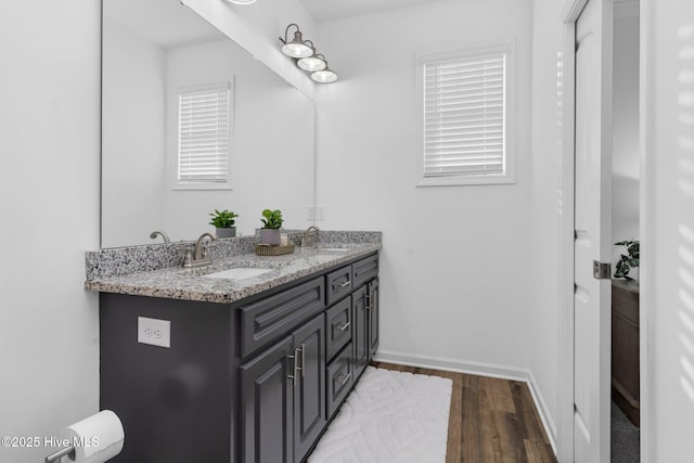 full bath with double vanity, baseboards, a sink, and wood finished floors