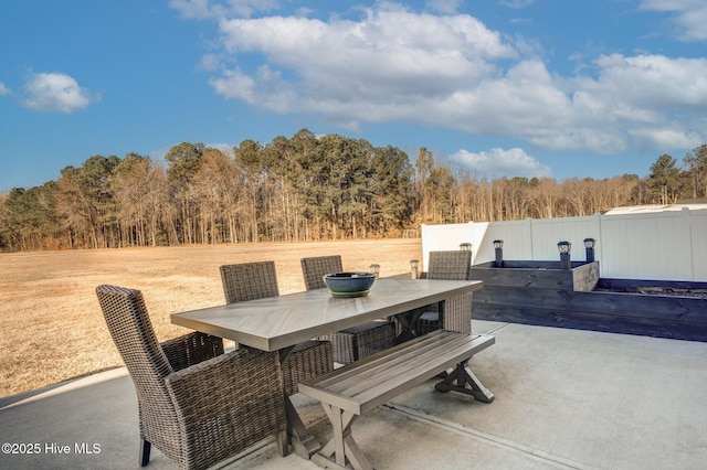 view of patio featuring outdoor dining area, fence, and a wooded view